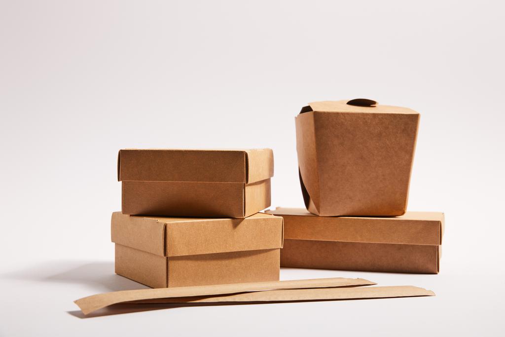 hůlky v papírových obalech v blízkosti odnášecí krabice s vařené čínské jídlo na bílém  - Fotografie, Obrázek