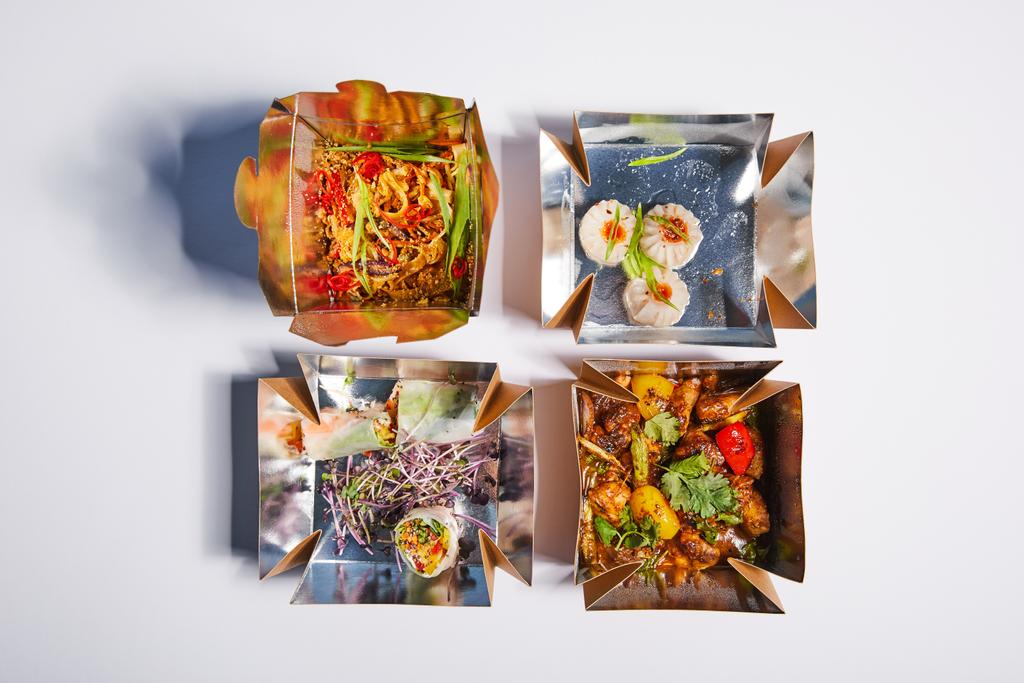 Blick von oben auf schmackhaftes und würziges chinesisches Essen in Take-away-Boxen auf weiß  - Foto, Bild