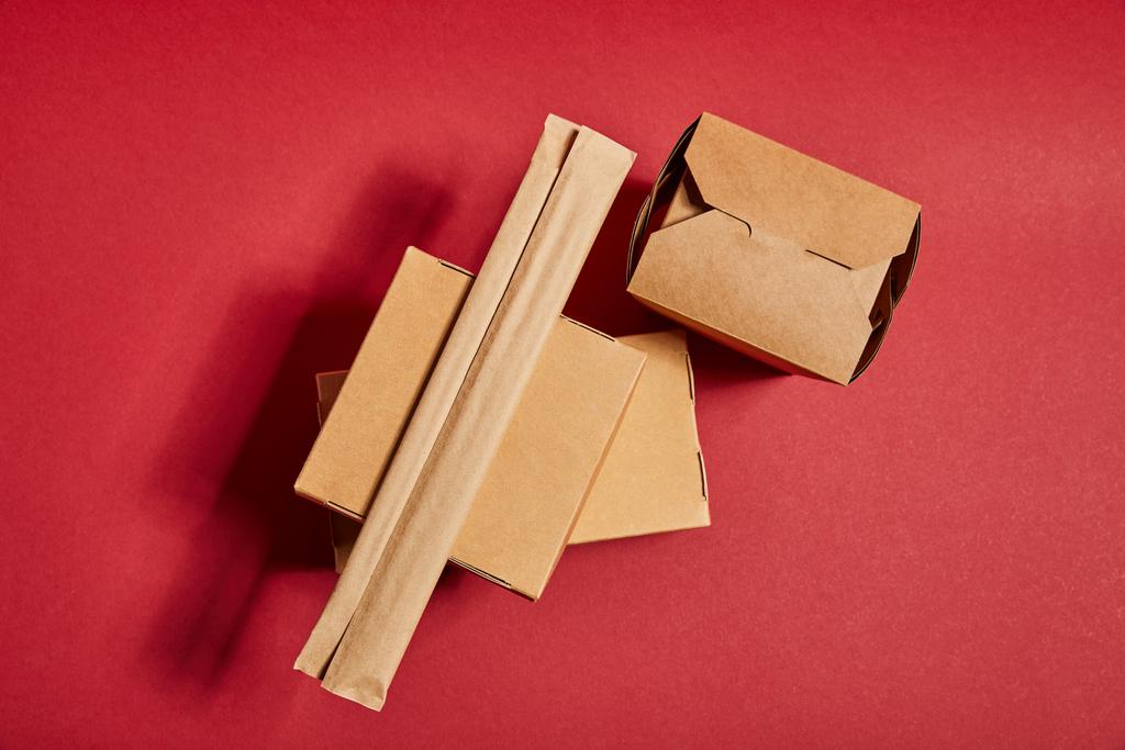 κορυφή άποψη των chopsticks σε χάρτινη συσκευασία κοντά κουτιά από χαρτόνι takeaway με παραδοσιακό κινέζικο φαγητό στο κόκκινο - Φωτογραφία, εικόνα