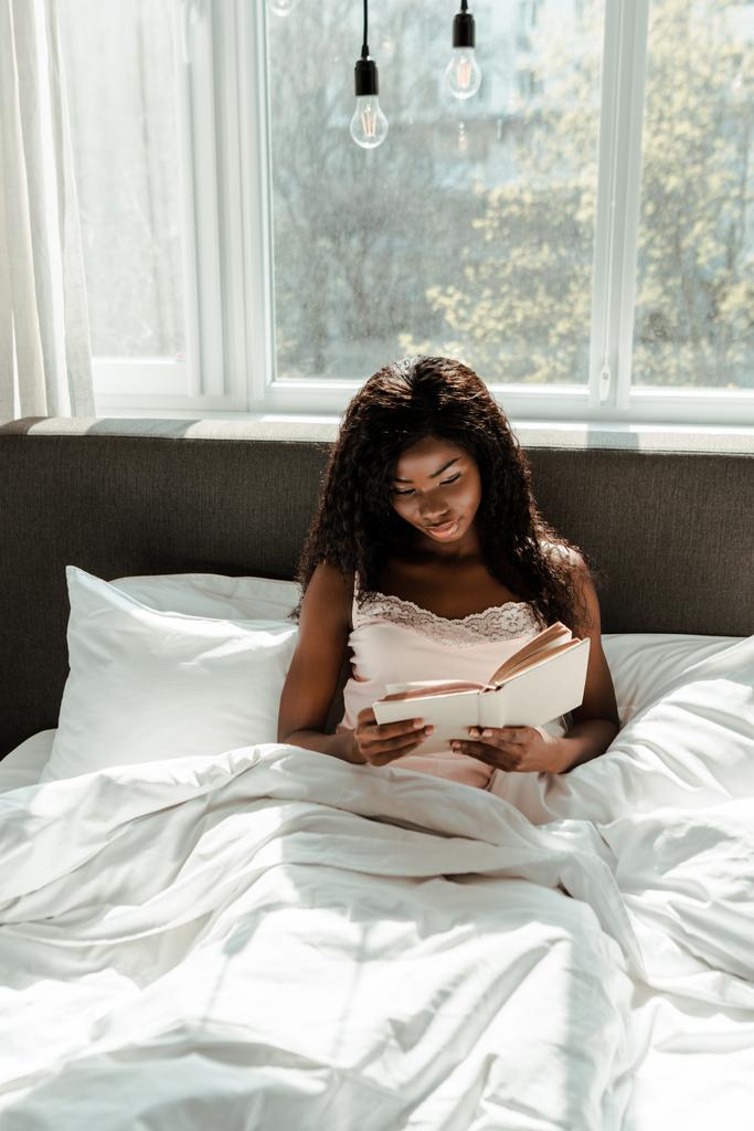 Mujer afroamericana leyendo libro en la cama en el dormitorio
 - Foto, imagen