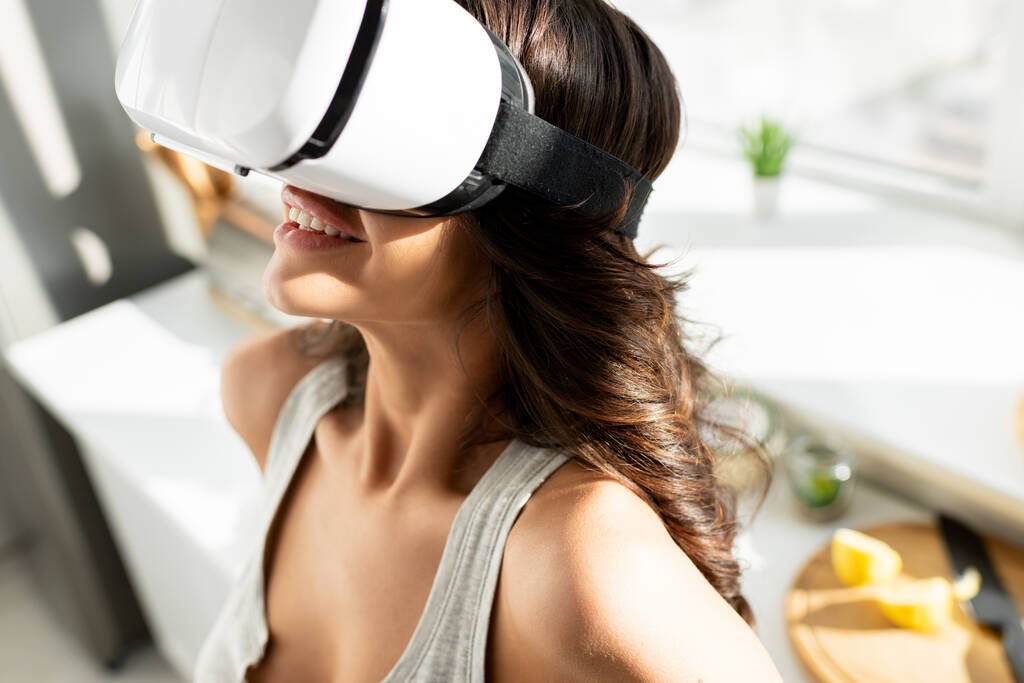 Улыбающаяся женщина с помощью гарнитуры виртуальной реальности на кухне
  - Фото, изображение