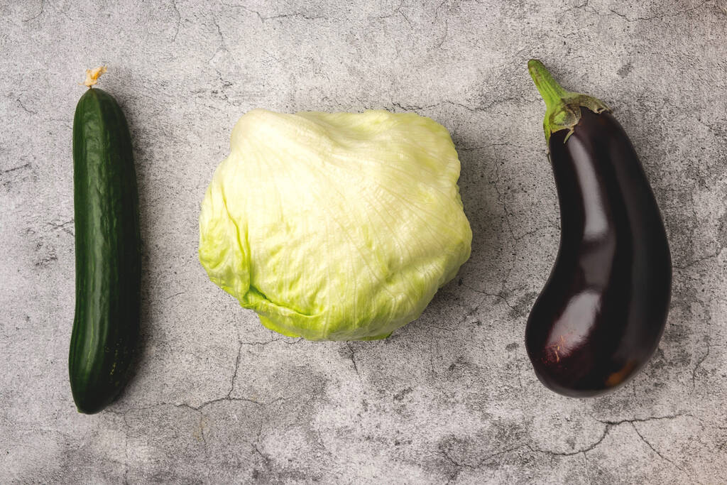 vegetables on a gray background: lettuce leaves, cucumber and eggplant, top view, copy space - Photo, Image