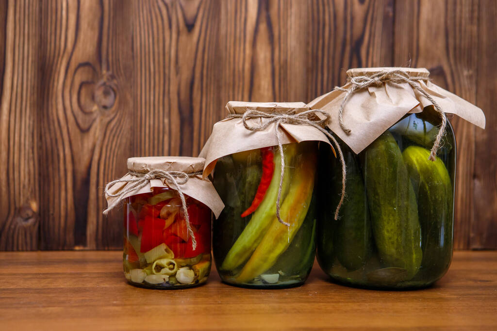 Κονσερβοποιημένα λαχανικά σε γυάλινα βάζα σε ξύλινο φόντο. Πίκλες. Αγγούρια και πιπεριές τουρσί. - Φωτογραφία, εικόνα