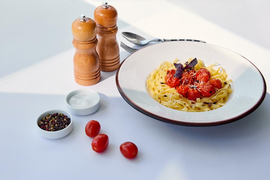 délicieuses pâtes aux tomates servies avec couverts, moulins à sel et poivre sur table blanche au soleil
 - Photo, image