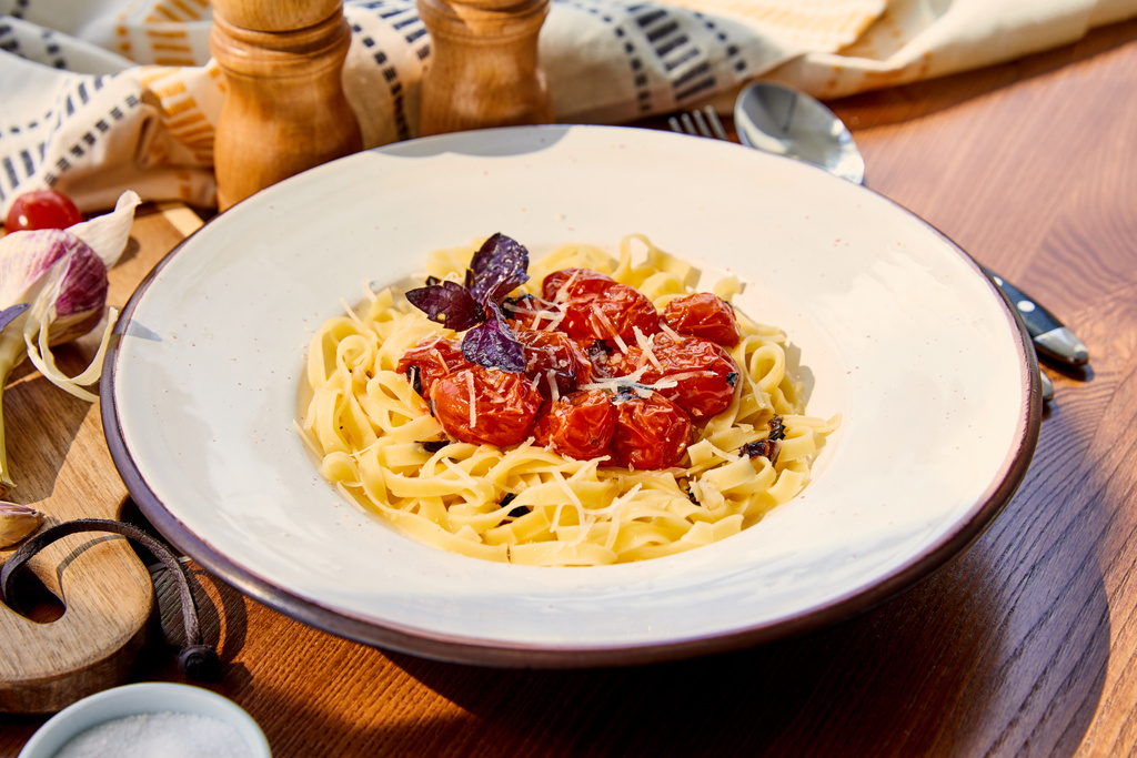 Güneş ışığında ahşap masada servis edilen domatesli, parmesanlı ve kırmızı fesleğenli lezzetli makarna. - Fotoğraf, Görsel