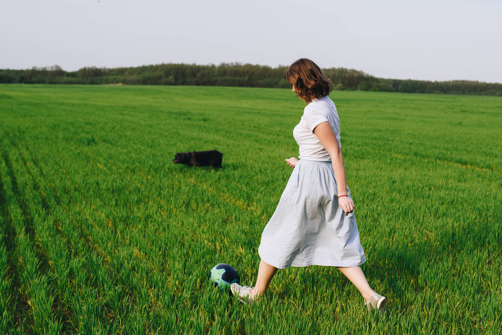Семья в лесу на прогулку. Пикник на лугу, на зеленой траве. Синяя одежда. Мама и сын играют в футбол. Животное. Чёрный пес. Мальчик в очках
. - Фото, изображение