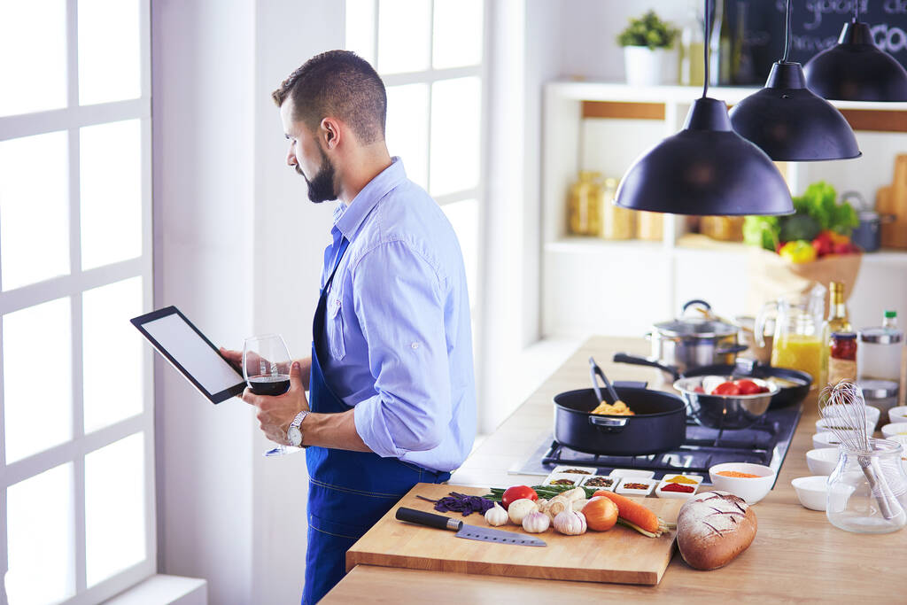 Muž po recept na digitální tablet a vaření chutné a zdravé jídlo v kuchyni doma - Fotografie, Obrázek