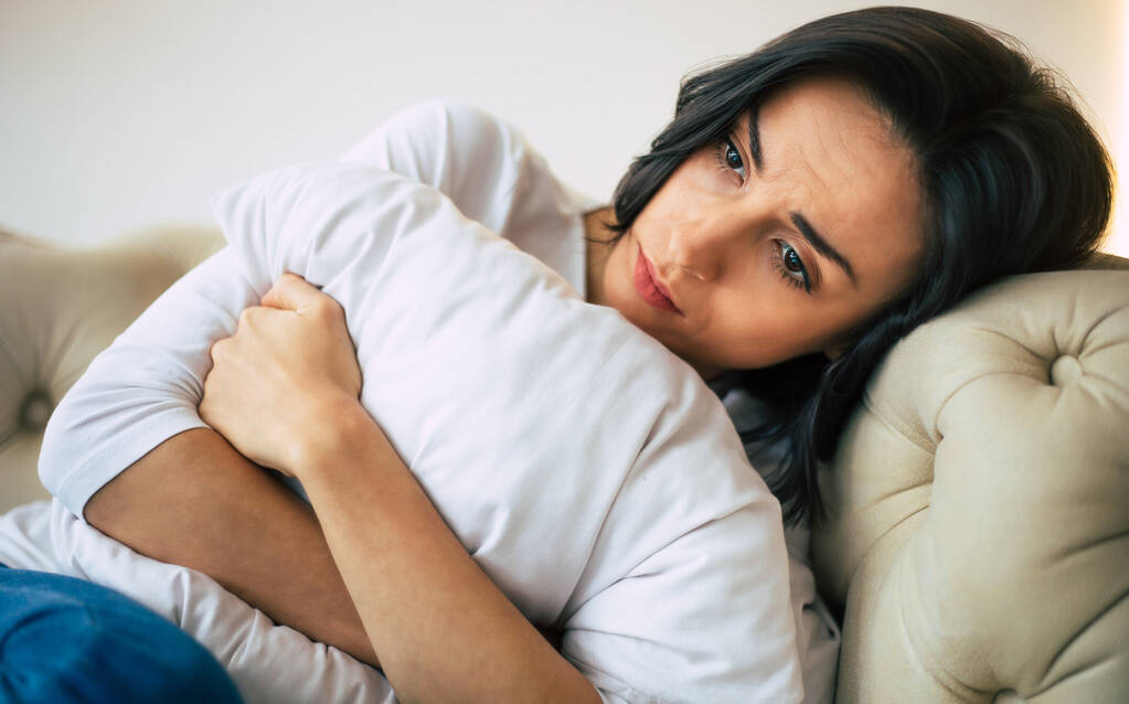 Mi sento male. Foto in primo piano di una giovane donna, che è sdraiata nel suo letto e abbraccia un cuscino, mentre si sente male
. - Foto, immagini