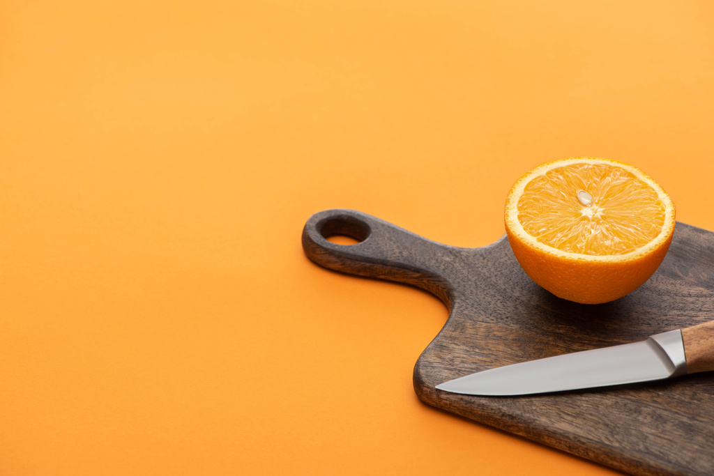 verse sappige oranje helft op snijplank met mes op kleurrijke achtergrond - Foto, afbeelding