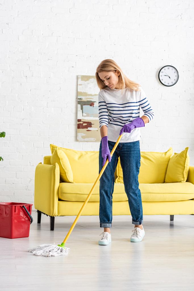 Donna in guanti di gomma pavimento di pulizia vicino secchio in soggiorno
 - Foto, immagini