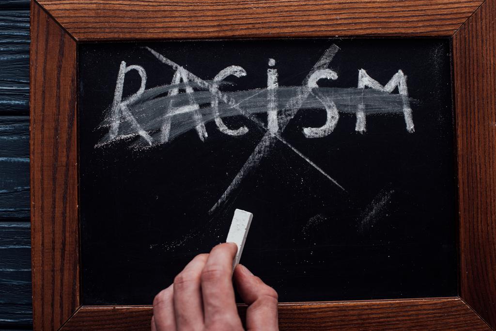 Vista dall'alto dell'uomo che tiene il gesso vicino alla lavagna con scritte razziste su sfondo di legno scuro
 - Foto, immagini