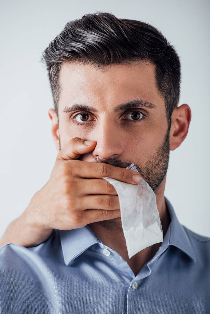 Αρσενικό χέρι εκμετάλλευση πακέτο με κοκαΐνη, ενώ καλύπτει το στόμα στον άνθρωπο που απομονώνονται σε γκρι - Φωτογραφία, εικόνα