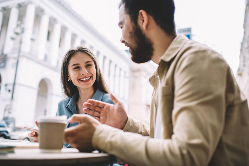 Radosny, zróżnicowany mężczyzna i kobieta przyjaciele śmieją się podczas komunikacji na żywo w kawiarni ulicznej, pozytywna dziewczyna czuje podekscytowany rozmową z partnerem w czasie wolnym na świeżym powietrzu - Zdjęcie, obraz