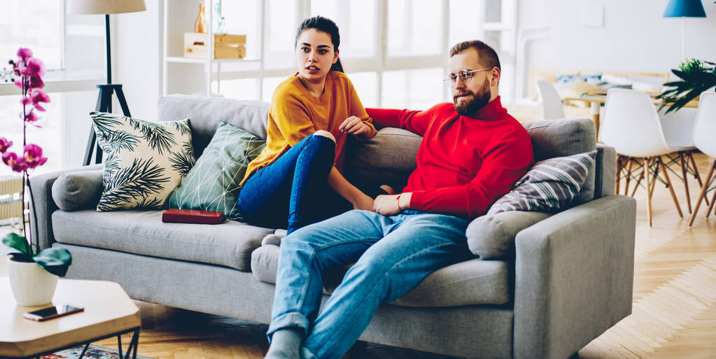 Houkutteleva valkoihoinen nainen katselee jotain istuu kodikas sohva vieressä aviomies asunnossa, romanttinen pari viettää vapaa-aikaa yhdessä mukava sohva moderni suunniteltu koti sisustus
 - Valokuva, kuva