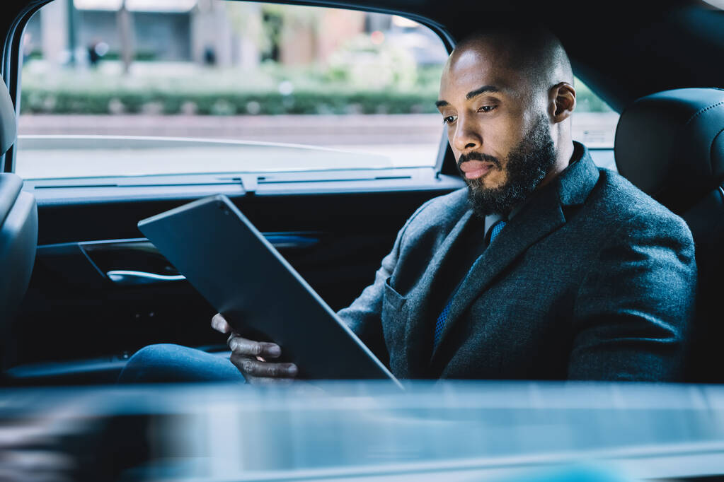 Homme d'affaires à la peau noire assis sur le siège arrière dans une voiture de taxi et à la recherche de numéro de contact pour faire une vidéoconférence en ligne via un pavé tactile moderne, concept de numérisation du marché sur tablette
 - Photo, image