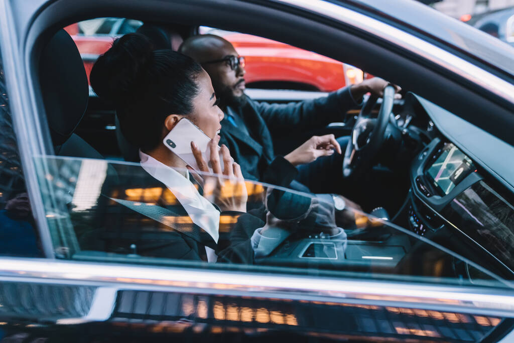 Mujer de negocios alegre sentado en el automóvil con conductor colega masculino y disfrutar de la conexión itinerante para hacer conversación celular internacional a través de una nueva aplicación de teléfono inteligente, asociación
 - Foto, Imagen