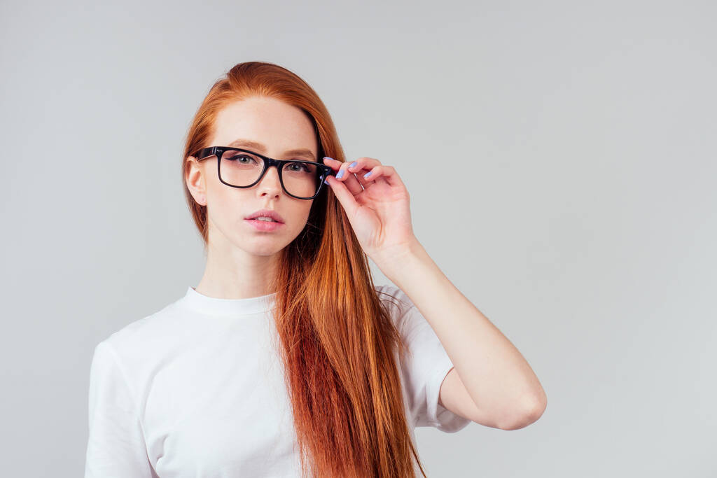 vörös hajú gyömbér nő visel szemüveg és fehér pamut öko-póló szürke stúdió háttér - Fotó, kép