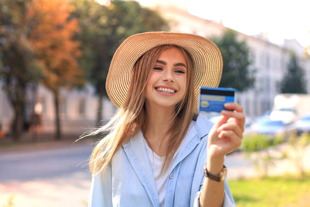 Jovem alegre otimista menina de pé ao ar livre, segurando cartão de crédito na mão
 - Foto, Imagem