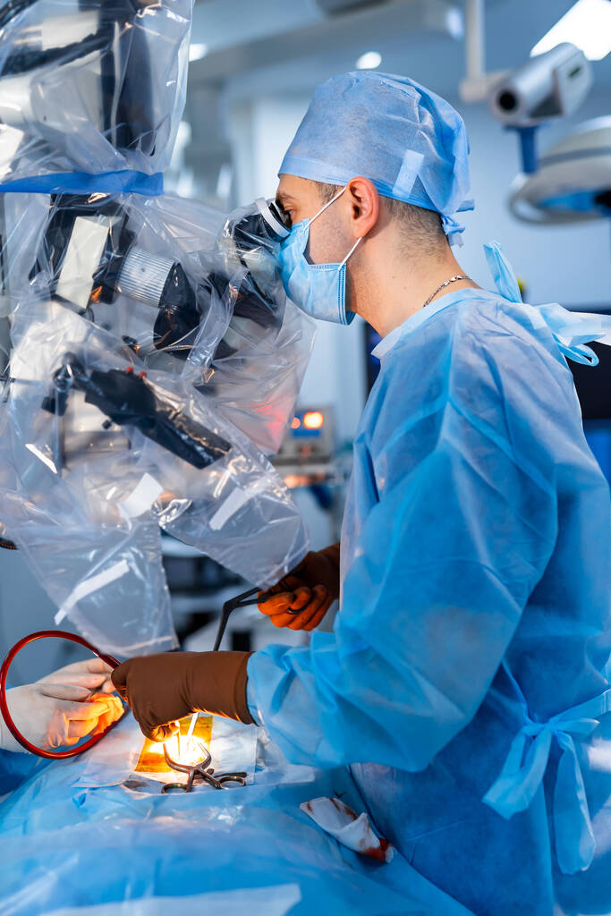 Spécialiste médical effectuant une chirurgie à l'aide d'équipements modernes. Profil du chirurgien masqué regardant au microscope dans la salle d'opération. - Photo, image