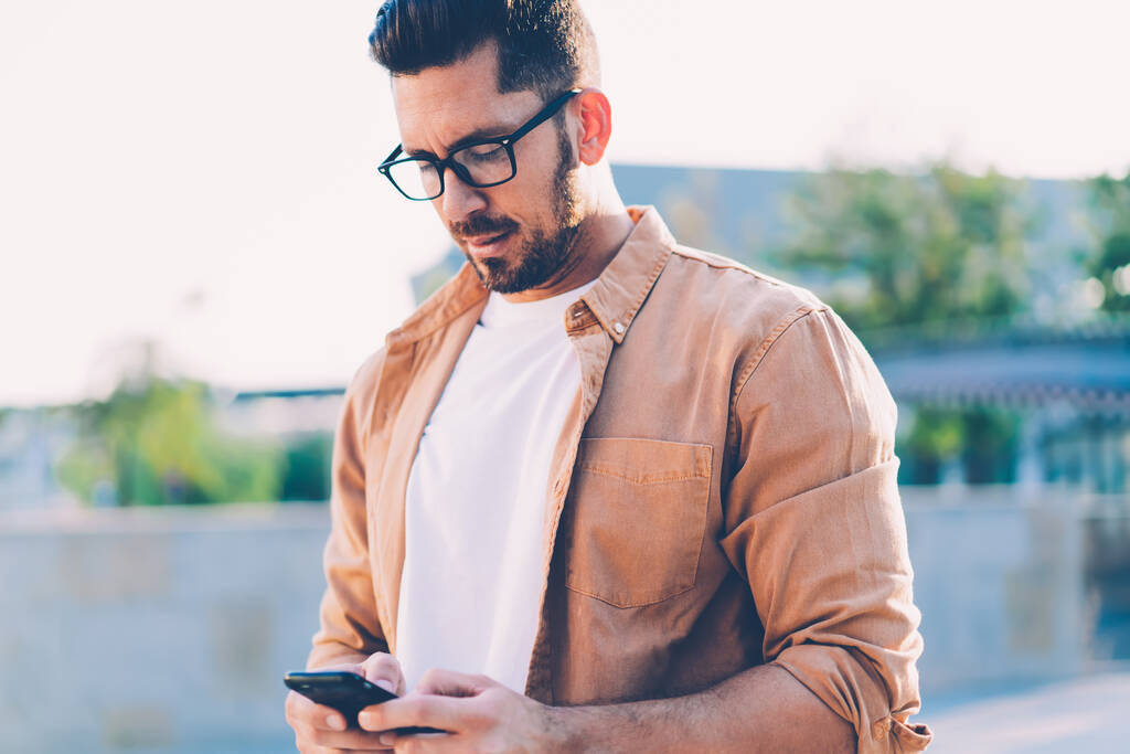 Handsome Caucasian man in spectacles for provide eyes protection typing text message via smartphone application connected to 4g wireless for browsing websites, concept of technology and communication - Photo, Image