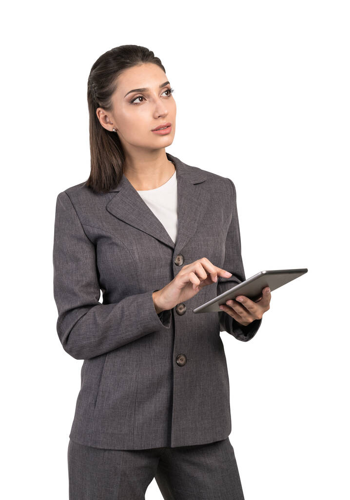 Odizolowany portret zamyślonej młodej bizneswoman w eleganckim garniturze przy użyciu komputera typu tablet. Pojęcie technologii i planowania - Zdjęcie, obraz