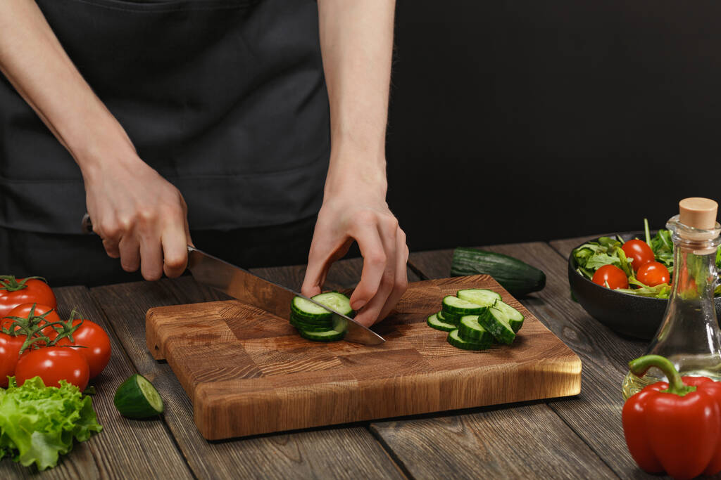 Žena vaří čerstvý zdravý salát. Ženské ruce řezání zeleniny na palubě na dřevěném stole s copyspace. - Fotografie, Obrázek