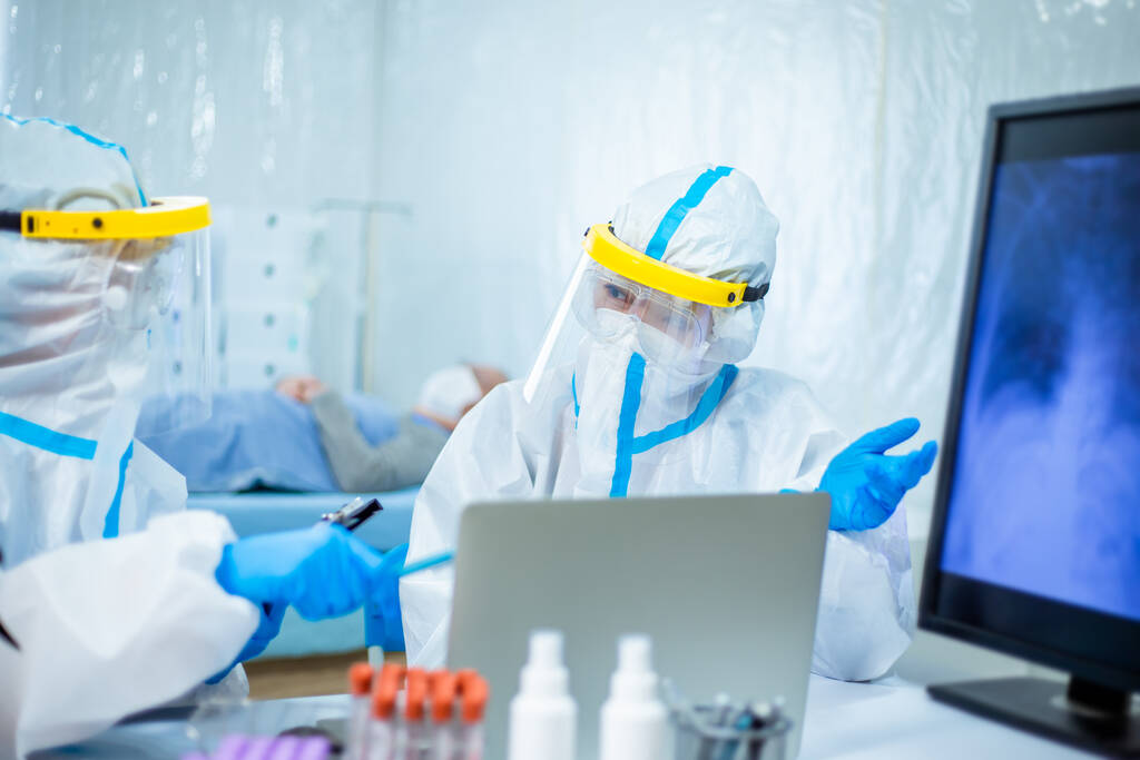 Ученые, изучающие рентген легких пациентов коронавируса на экране компьютера в изолированном платье или защитных костюмах и хирургических масках для лица
 - Фото, изображение