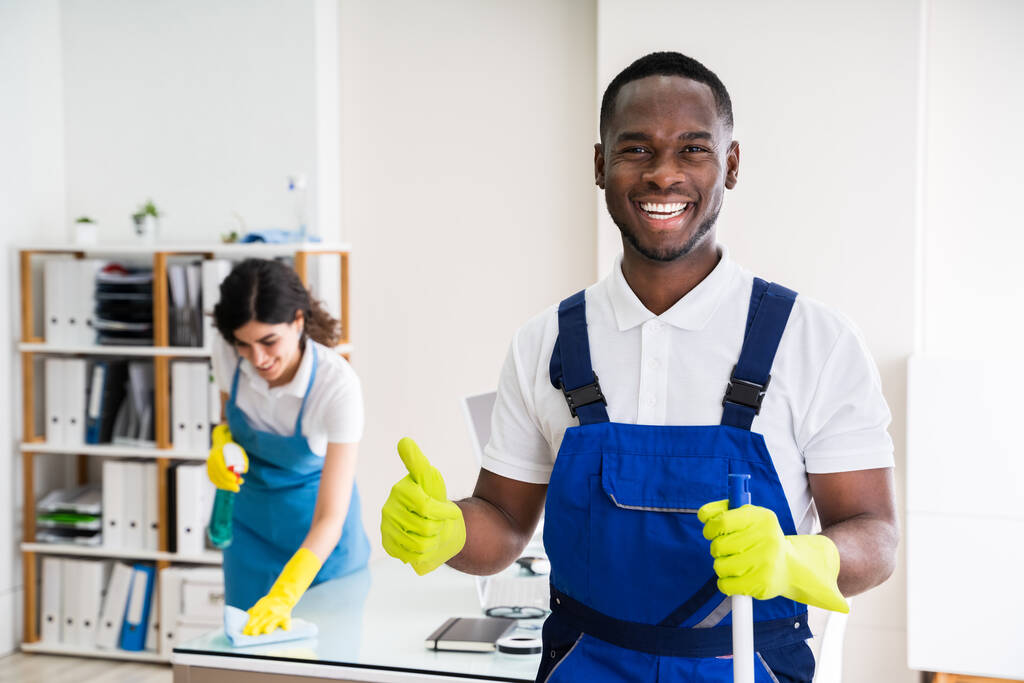 Retrato de um homem feliz zelador com equipamento de limpeza no escritório
 - Foto, Imagem
