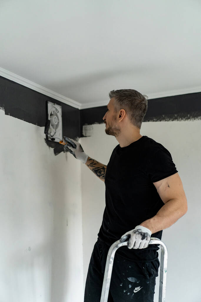 réparations. l'homme peint les murs avec un rouleau, se prépare pour la peinture, les réparations dans la pièce. repeindre le mur
. - Photo, image