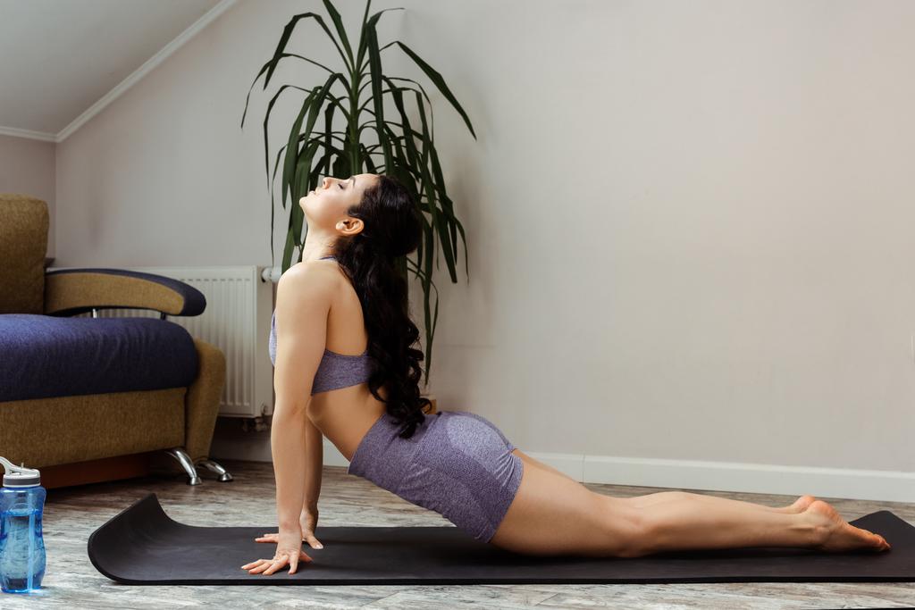 attraktives sportliches Mädchen, das während der Selbstisolierung zu Hause auf einer Yogamatte übt - Foto, Bild