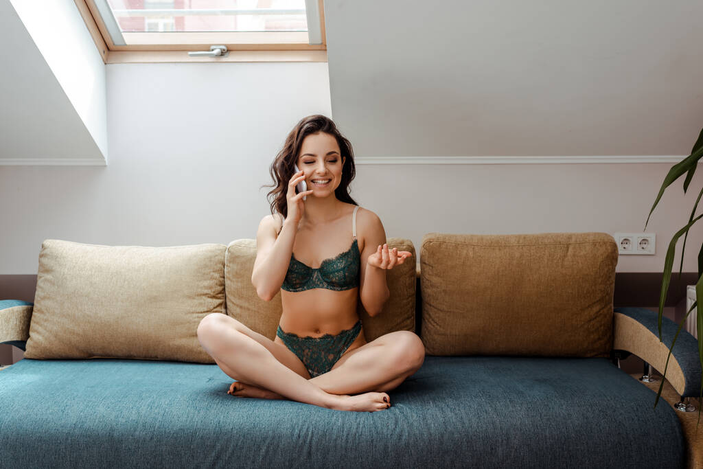 atractiva chica sexy en lencería hablando en el teléfono inteligente mientras está sentado en el sofá en casa
 - Foto, Imagen