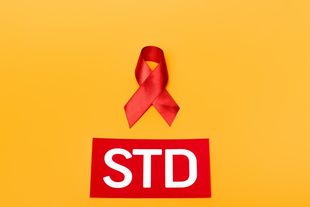 felső nézet a piros szalag, mint a HIV-tudatosság közelében STD betű elszigetelt narancs  - Fotó, kép
