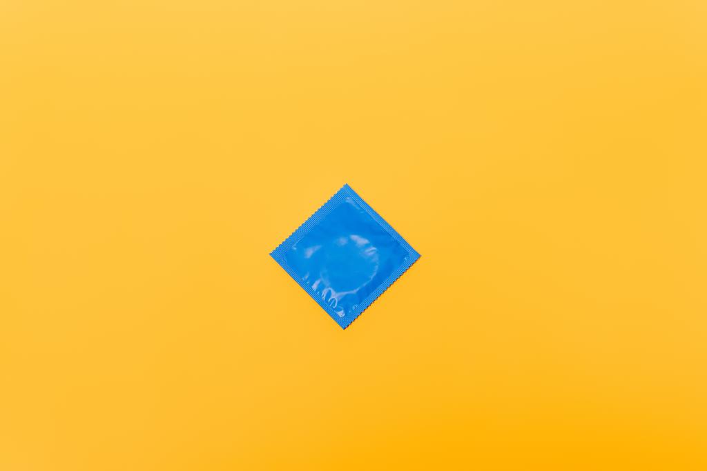 bovenaanzicht van blauwe verpakking met condoom geïsoleerd op oranje - Foto, afbeelding
