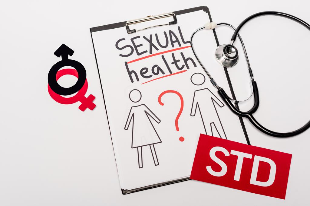 верхний вид буфера обмена с надписью сексуального здоровья, нарисованные мужчина и женщина рядом стетоскоп, гендерные признаки и STD изолированы на белом
  - Фото, изображение