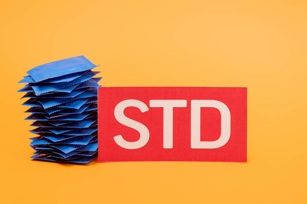 stapel condooms bij papier met std letters geïsoleerd op oranje  - Foto, afbeelding