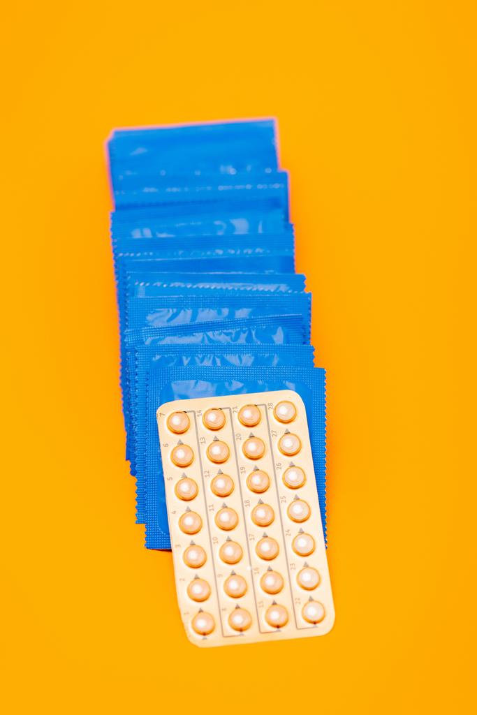 κορυφαία άποψη των αντισυλληπτικών χαπιών κοντά σε συσκευασίες με προφυλακτικά που απομονώνονται σε πορτοκαλί  - Φωτογραφία, εικόνα