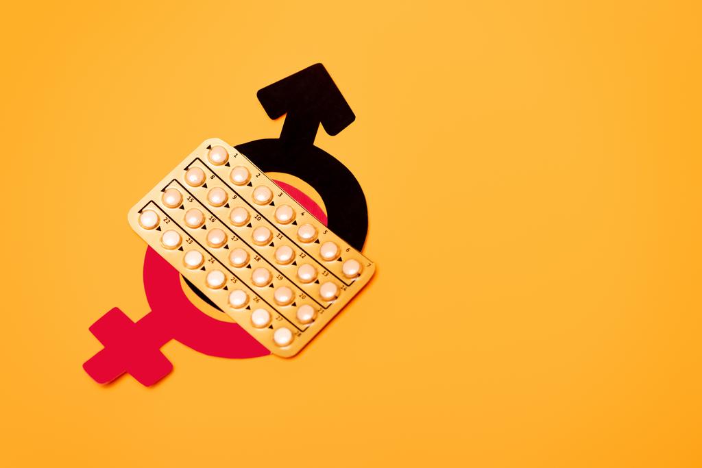 widok z góry blistra z tabletkami antykoncepcyjnymi i symbolami płci wyizolowanymi na pomarańczowym  - Zdjęcie, obraz