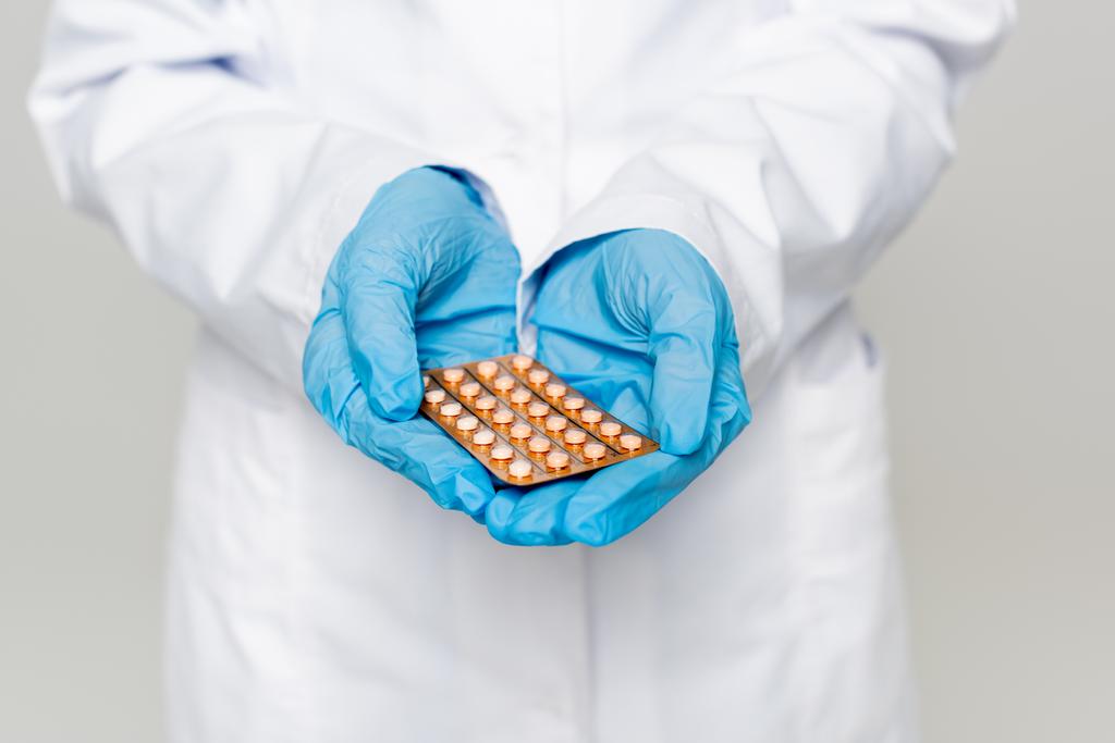 обрізаний вид лікаря, який тримає блістерну упаковку з контрацептивними таблетками ізольовані на сірому
  - Фото, зображення