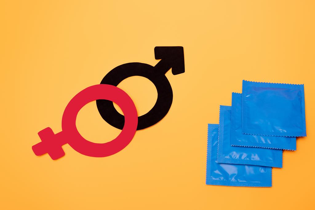 Turuncu üzerine izole edilmiş prezervatiflerin yakınındaki cinsiyet sembollerinin üst görünümü - Fotoğraf, Görsel