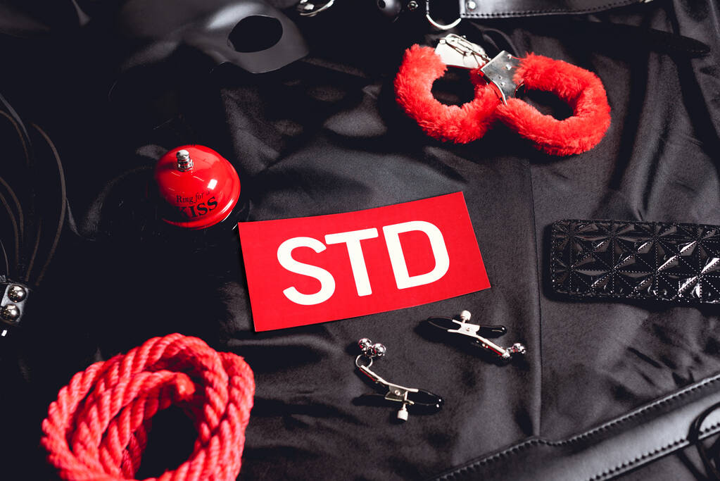 верхний вид секс-колокол рядом с бумагой с надписью STD и секс-игрушки на черном
 - Фото, изображение