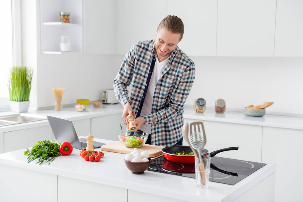 Photo of positive cheerful proper nutrition lover make veggie supper salt pepper fresh tomato lettuce cabbage salad wear checkered plaid shirt in kitchen house indoors - Photo, Image