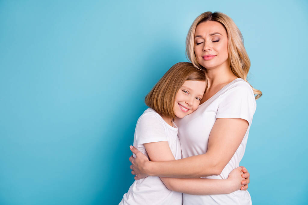 Foto de perfil de dos personas joven hermosa mamá señora pequeña hija rubia abrazando los ojos cerrados de las manos llevar casual blanco s-camisas aisladas de color azul de fondo
 - Foto, Imagen