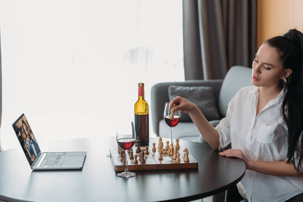 jeune femme jouant aux échecs lors d'un appel vidéo avec petit ami près de vin rouge sur la table
 - Photo, image