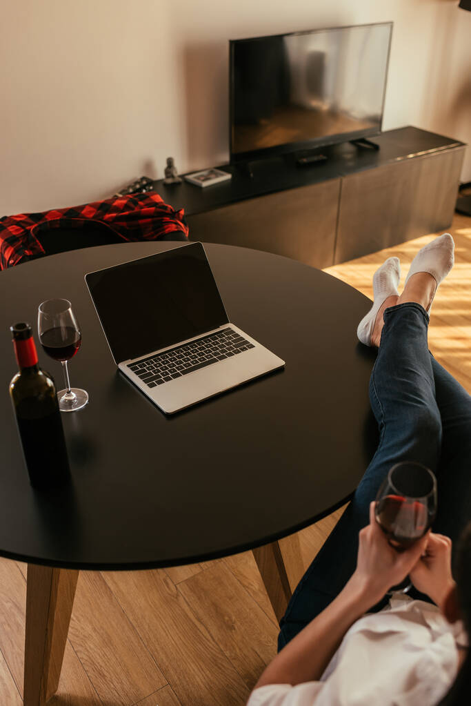 Dizüstü bilgisayarın yanında boş ekranlı bir masada oturmuş şarap kadehi tutan bir kadının görüntüsü. - Fotoğraf, Görsel