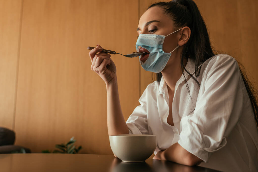 fiatal nő orvosi maszk lyuk reggelizik otthon - Fotó, kép