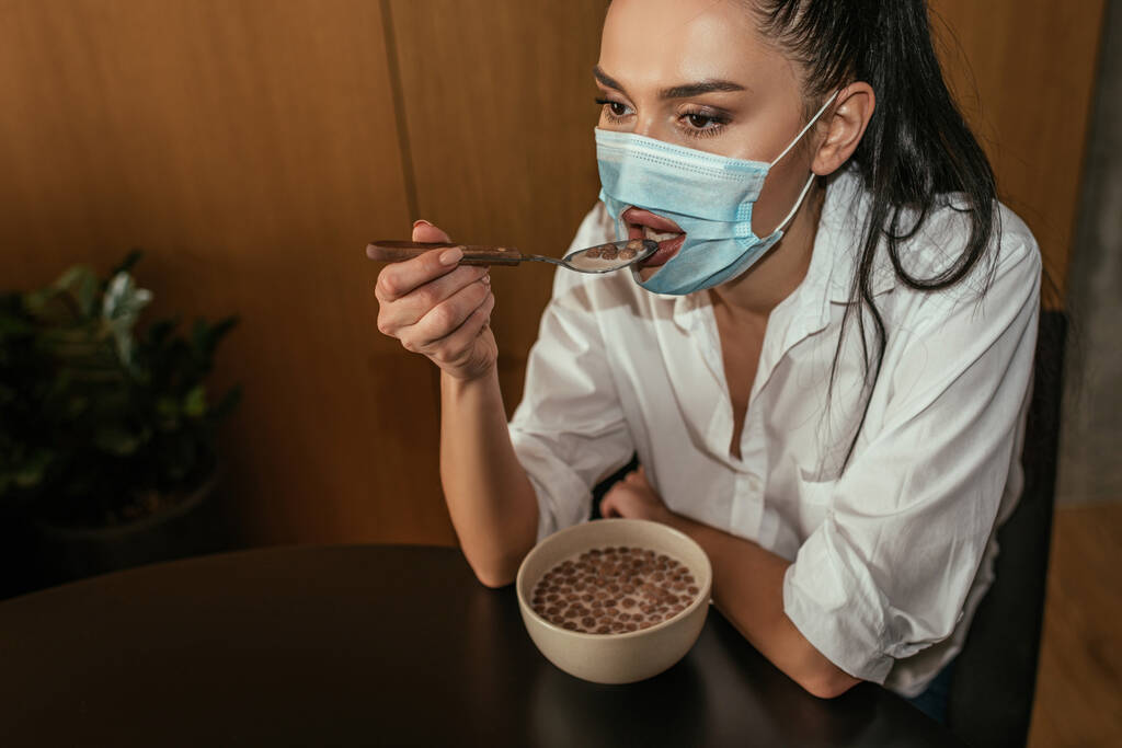депрессивная женщина с дыркой в медицинской маске завтракает дома
 - Фото, изображение