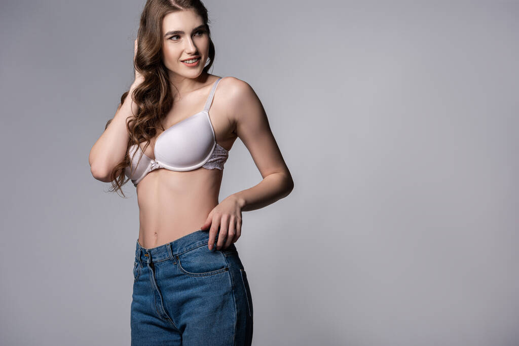 happy girl in bra and denim jeans standing on grey  - Photo, Image