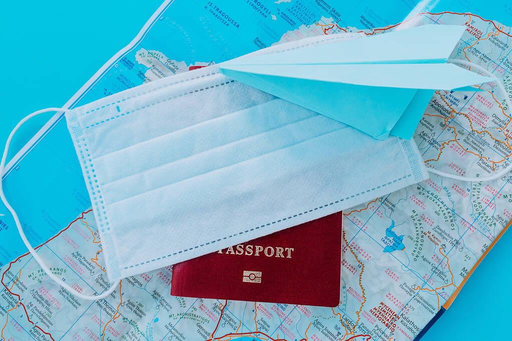 Blauw papieren vliegtuig, paspoort en beschermmasker op de achtergrond van een kaart van Griekenland Concept van een vliegverbod als gevolg van een coronavirus pandemie. - Foto, afbeelding