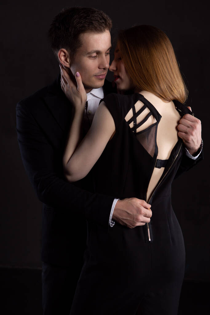 Ένας κομψός άντρας ξεκουμπώνει το φόρεμα μιας κοπέλας που τον φιλάει, εκθέτοντας την λεπτή σέξι πλάτη της. Το κορίτσι χαϊδεύει απαλά το μάγουλο του άντρα κατά τη διάρκεια ενός φιλιού - Φωτογραφία, εικόνα