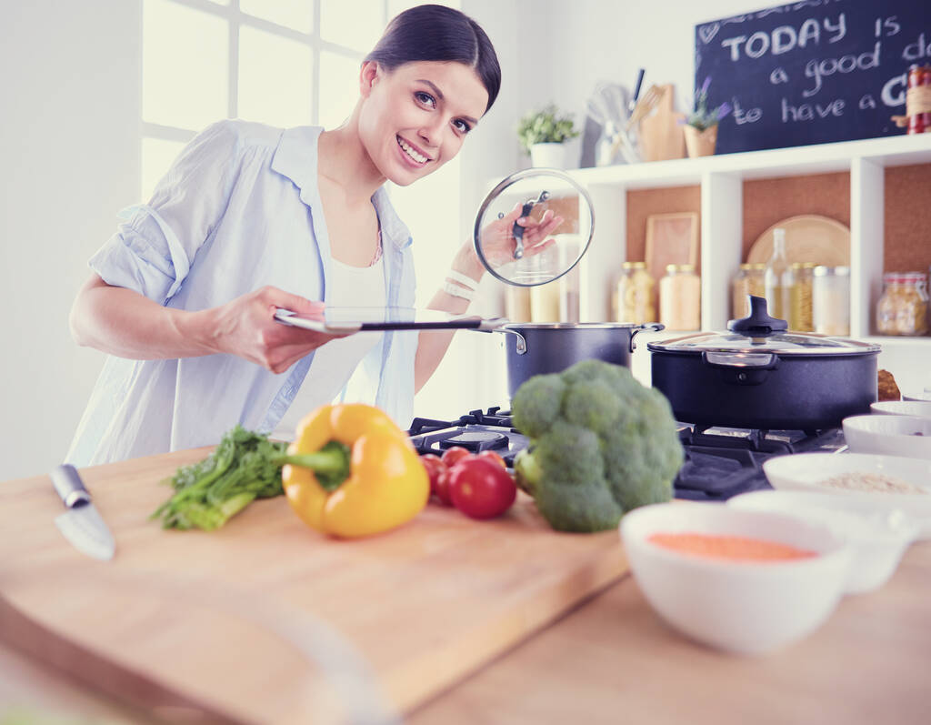 Νεαρή γυναίκα στέκεται δίπλα στη σόμπα στην κουζίνα - Φωτογραφία, εικόνα